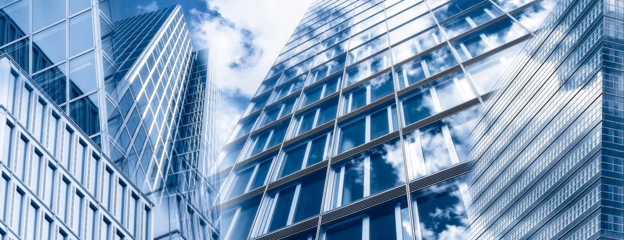 LUBA Immobilien UG – Immobilien – Ansicht von unten auf moderne Glaswolkenkratzer, die Wolken im blauen Himmel spiegeln