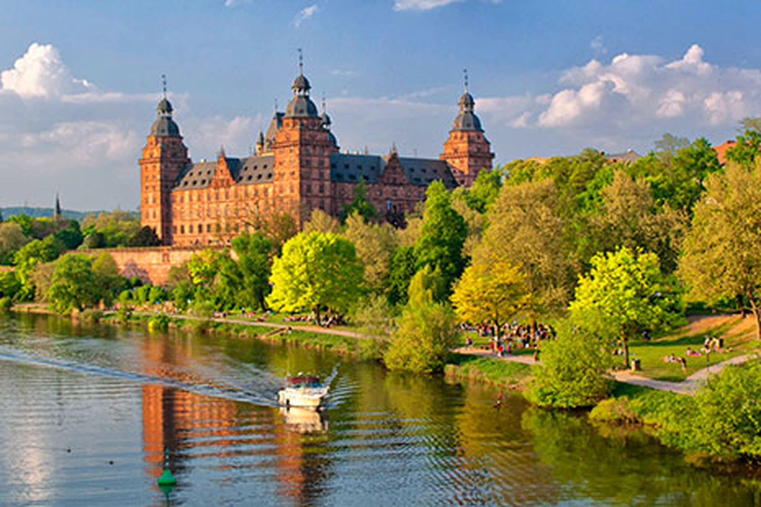 LUBA Immobilien UG - Immobilien - Großes historisches Schloss mit vier Türmen in der Nähe eines Flusses, mit grünen Bäumen am Flussufer und einem Boot auf dem Wasser
