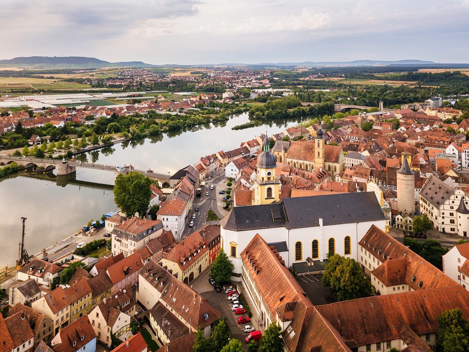 LUBA Immobilien UG – Immobilien – Luftaufnahme einer europäischen Stadt mit einem Fluss, der hindurchfließt, mit historischen Gebäuden, einer Kirche mit Glockenturm und einer Steinbrücke