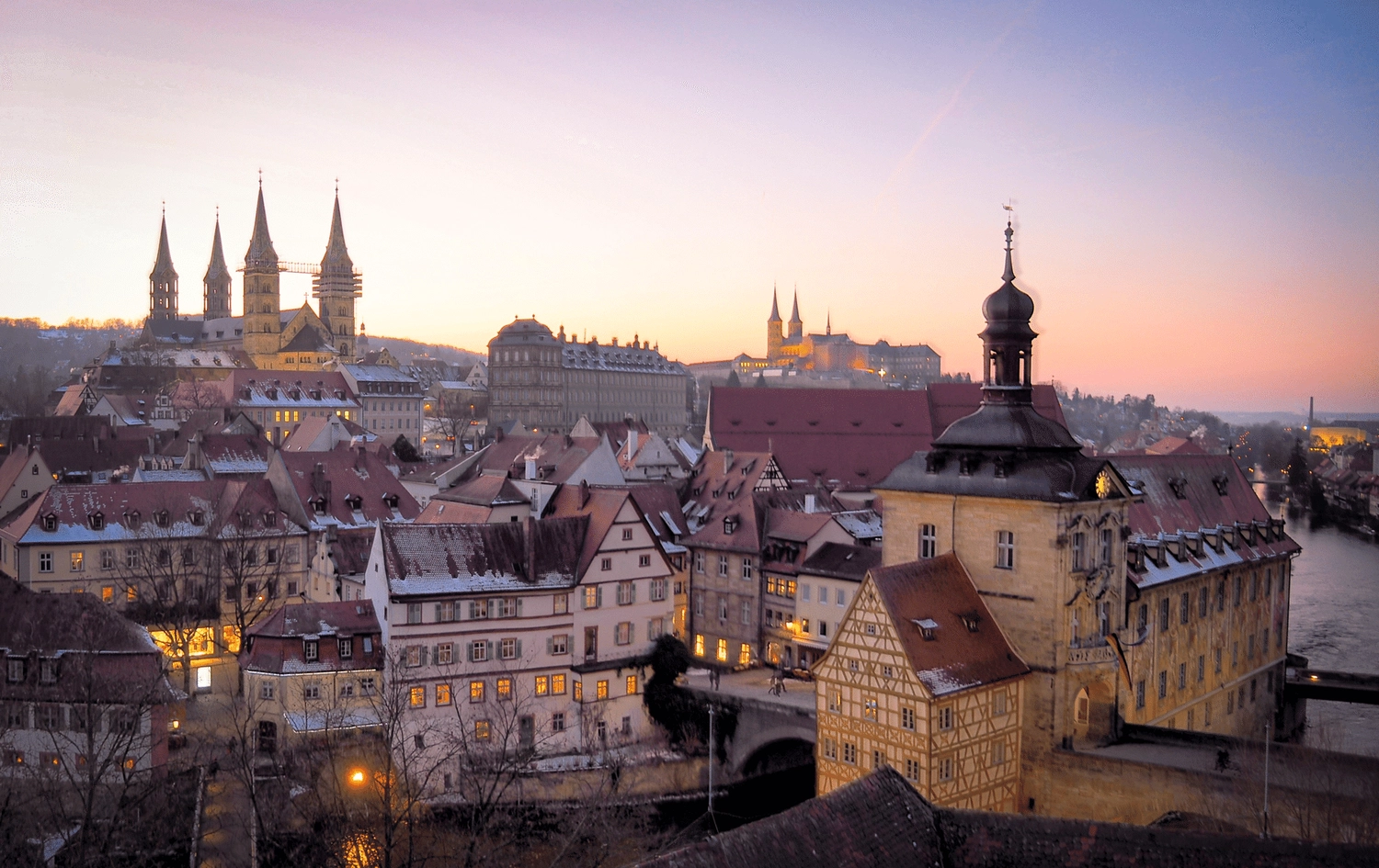 LUBA Immobilien UG – Immobilien – Panoramablick auf die Bamberger Stadt mit beleuchteten historischen Gebäuden, Kirchtürmen und dem Fluss bei Sonnenuntergang